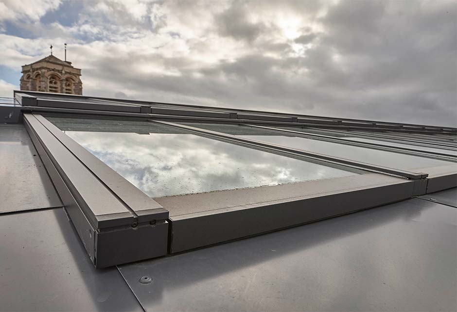 Afbeelding van buitenkant van de step lessenaarsdak oplossing, gezien vanaf het dak. Reflectie van wolken in het glas.